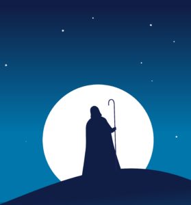 Guy in hooded cloak with a stick walking to a village in the night.